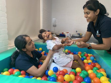 Child in ball pit during occupational therapy session at cpotential, with two multidisciplinary therapists.